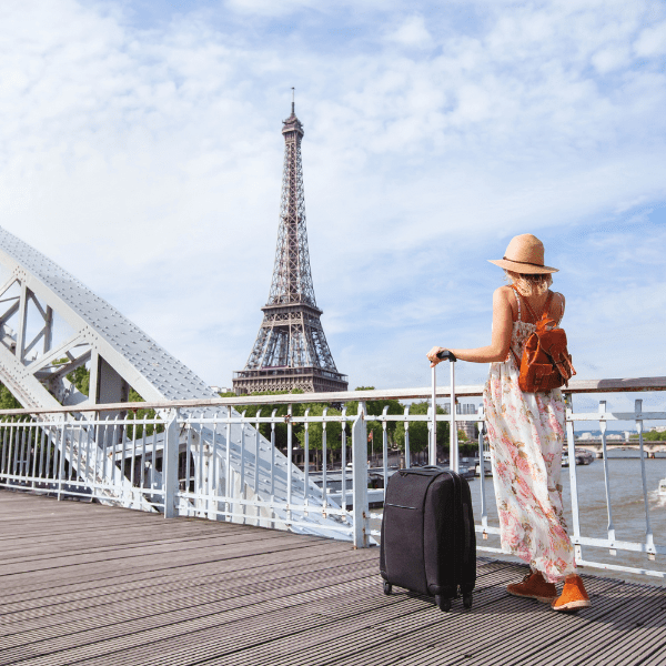Femme avec une valise sur un pont au dessus de la Seine face à la Tour Eiffel